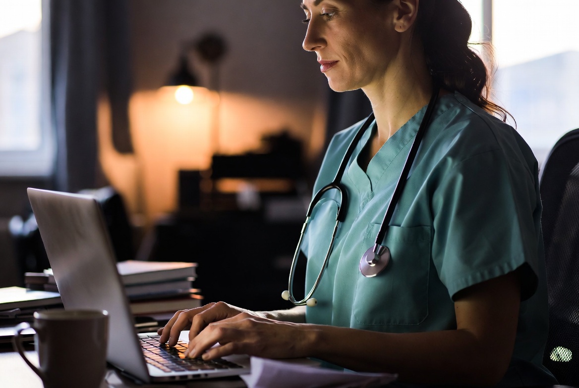 Nurse in scrubs studying online from home using a laptop, representing flexible online nursing programs.